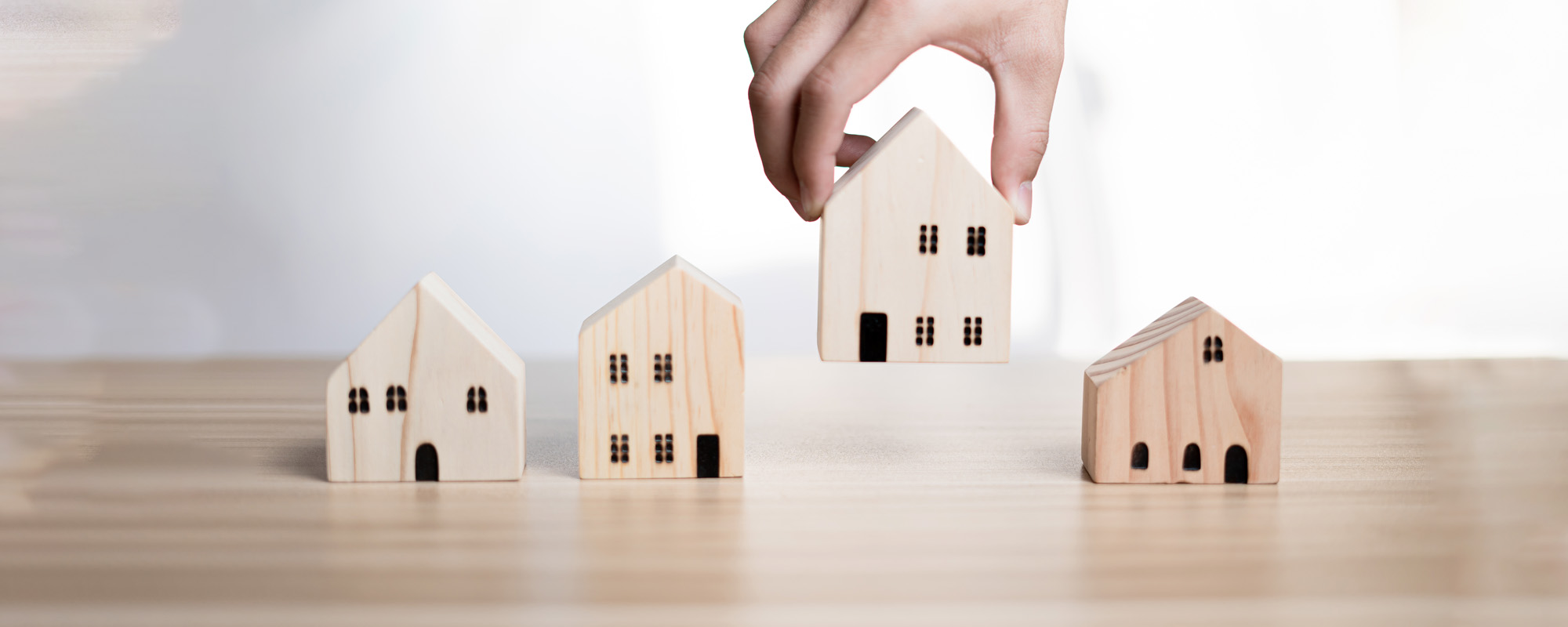 businessman holding a wooden house placed on a table