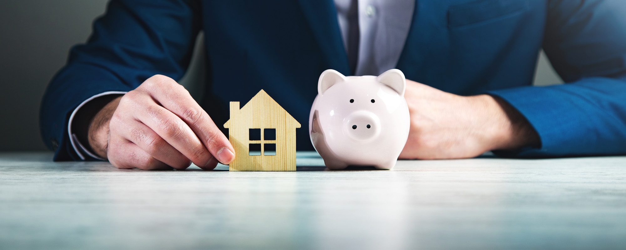 businessman holding wooden house and piggy bank